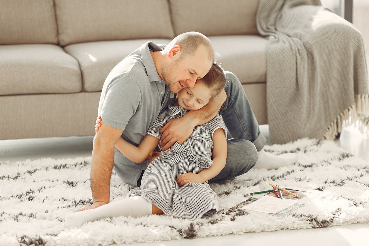 Heartwarming moment of father hugging daughter on a rug in a bright living room.