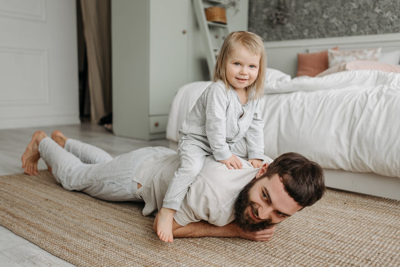 Father and daughter playing together in a cozy, light-filled bedroom, creating a warm family moment.